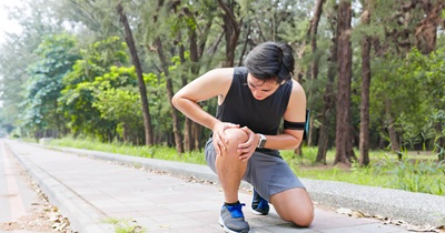 A man kneels on the ground, showing discomfort while clutching his knee in pain.