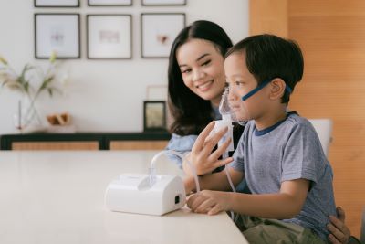 A mother assisting her child in using an OMRON compressor nebulizer for respiratory treatment.
