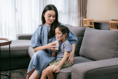A mother assisting her child in using an OMRON mesh nebulizer for respiratory treatment.